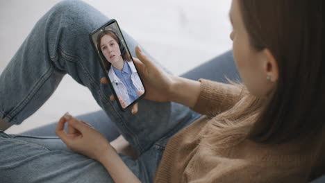 Female-medical-assistant-wears-white-coat-headset-video-calling-distant-patient-on-smartphone.-Doctor-talking-to-client-using-virtual-chat-telephone-app.-Telemedicine-remote-healthcare-services